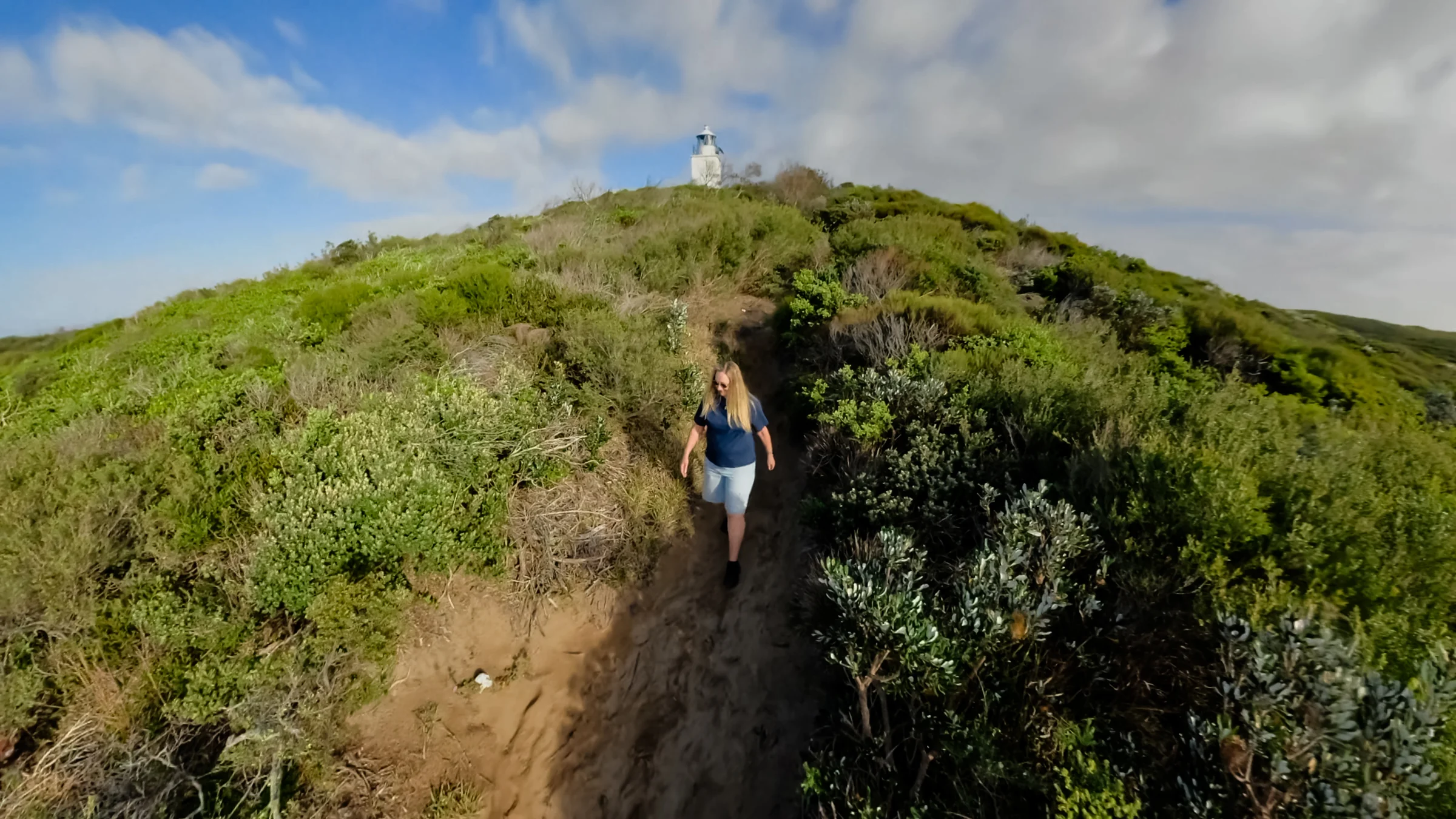 Sue walking along the path through dense green coastal heath