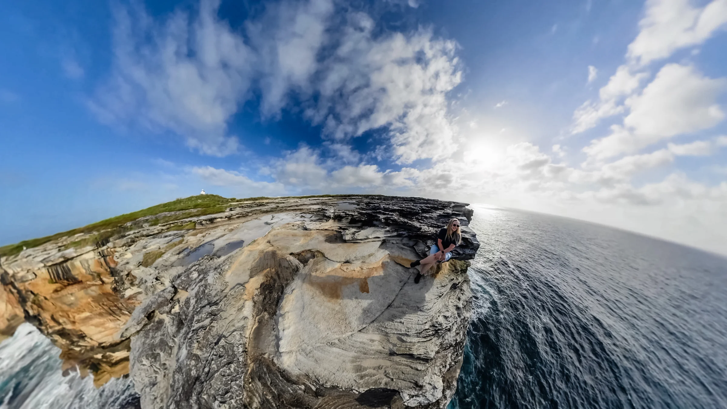 Curved wide-angle view of sandstone cliff tops with ocean beyond