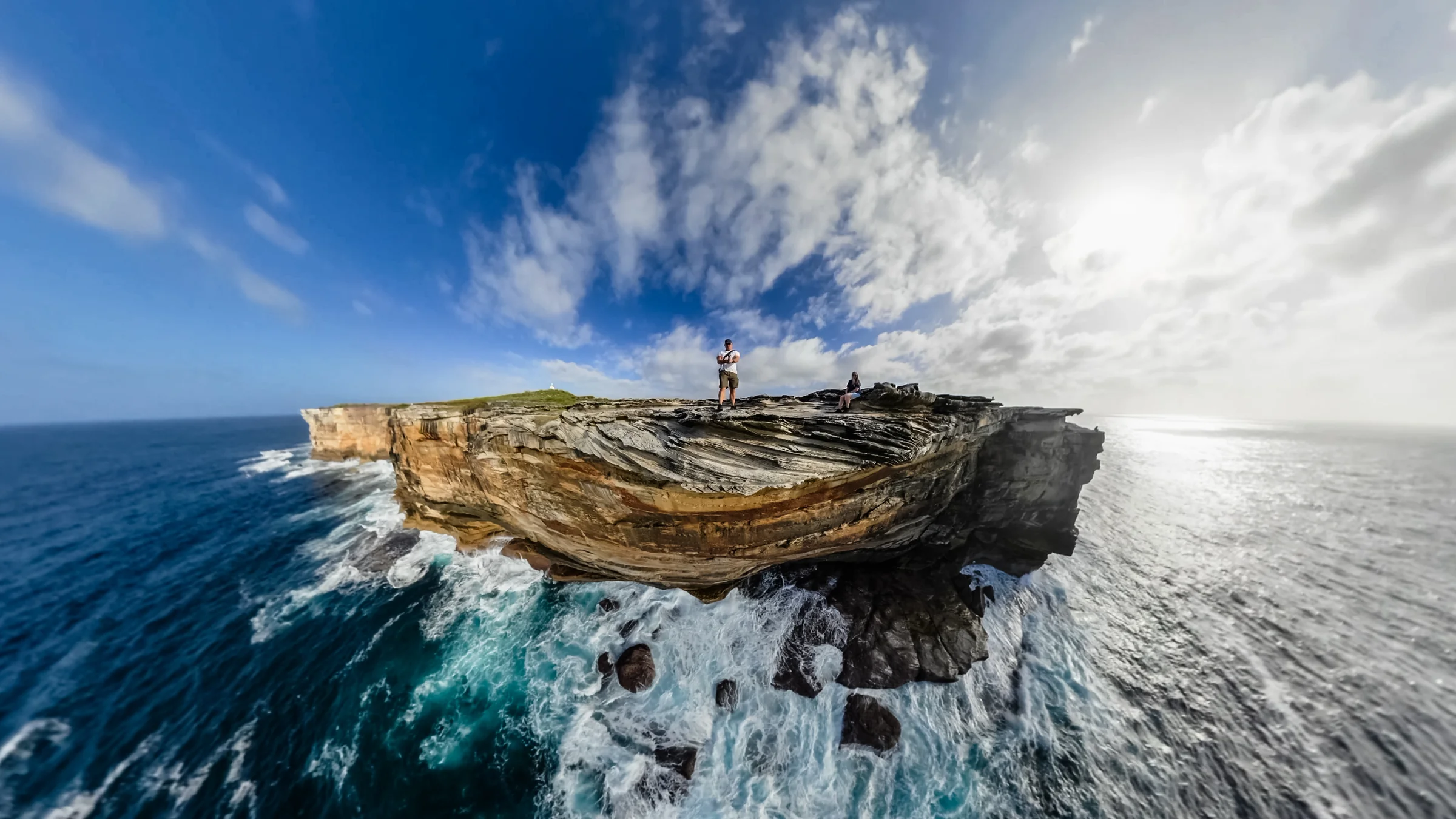 Wide-angle view of Rob and Sue on sandstone with waves below