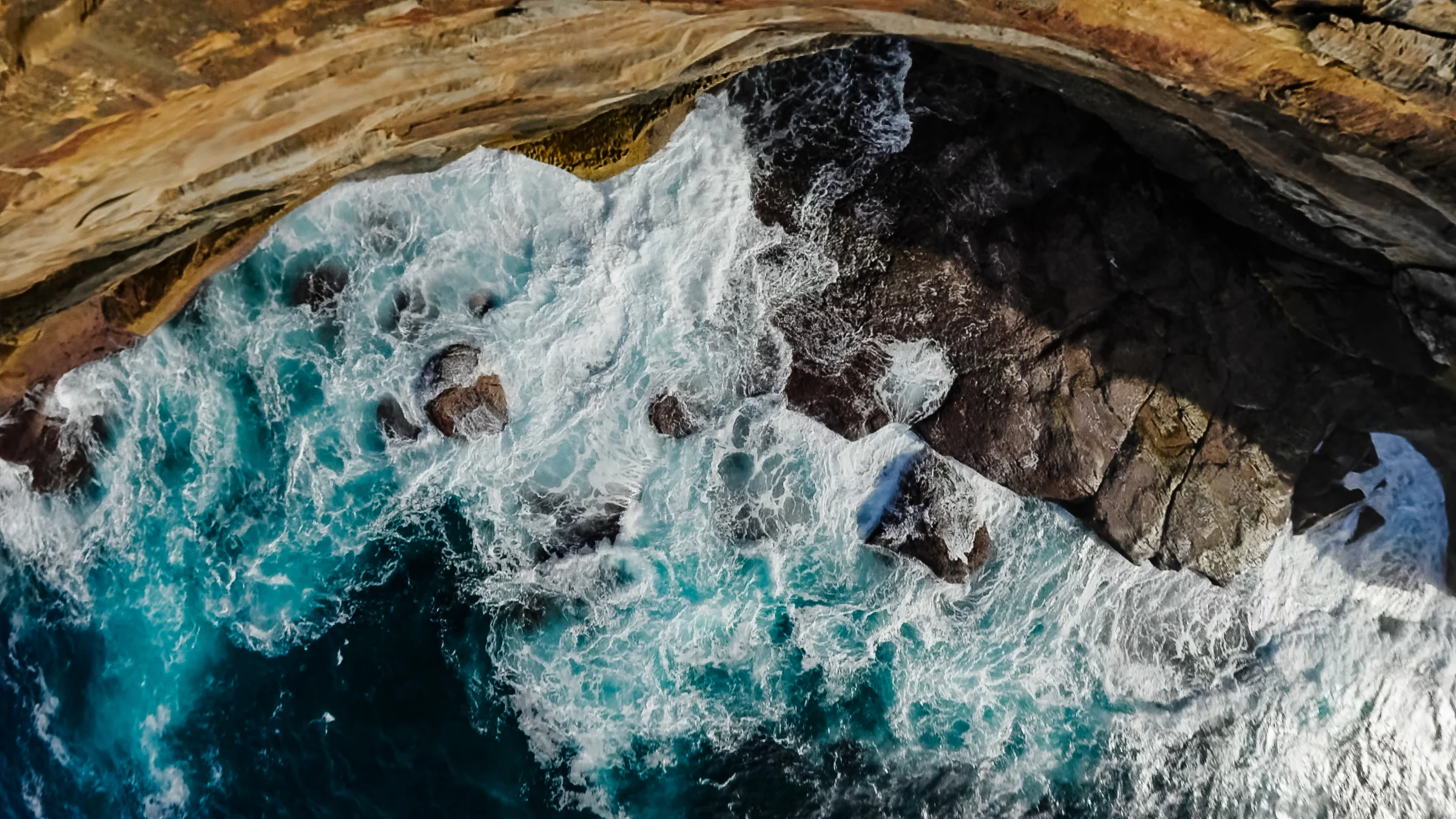 Waves washing against layered sandstone below the cliffs