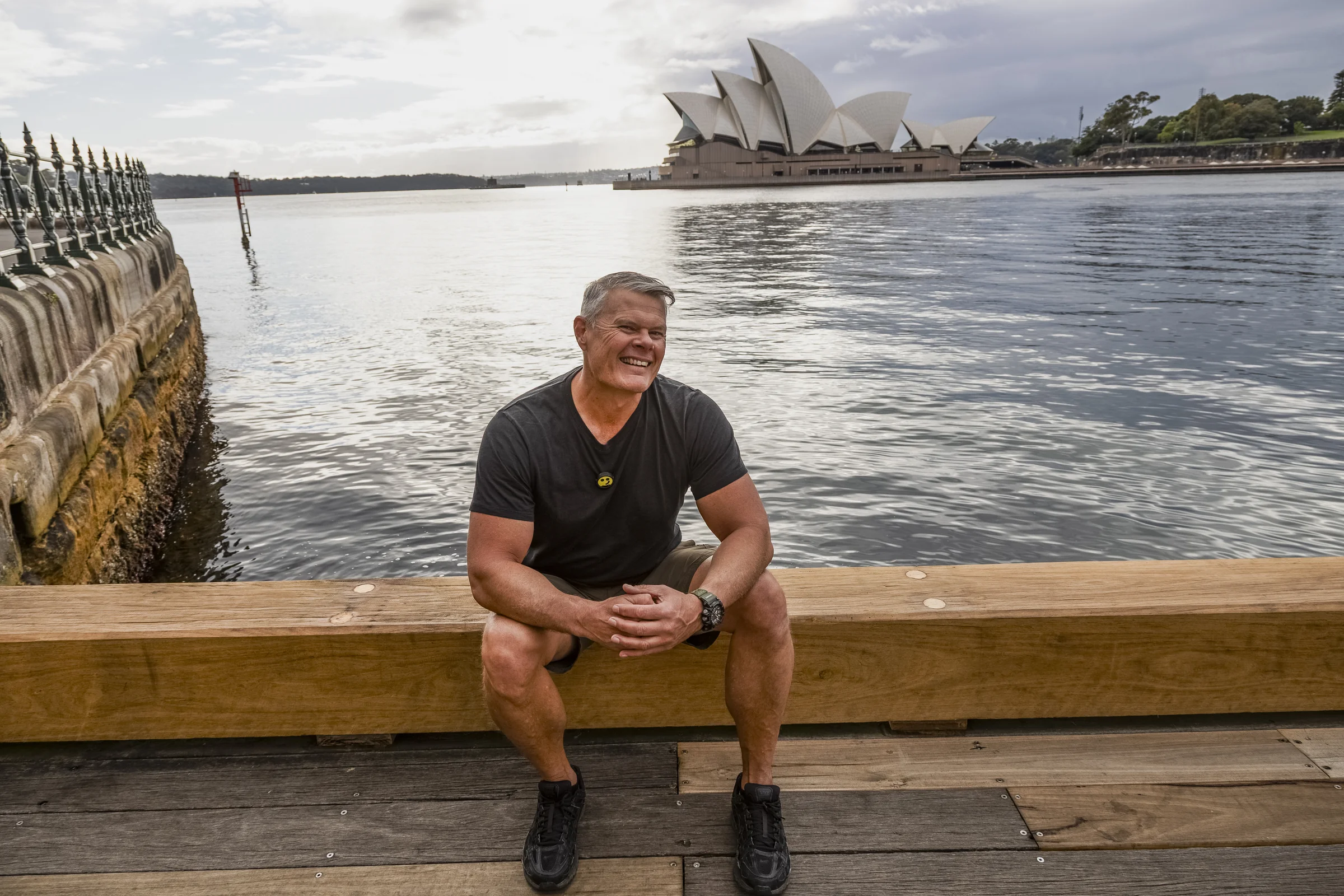 Rob sitting beside the waterfront with the Opera House across the harbour