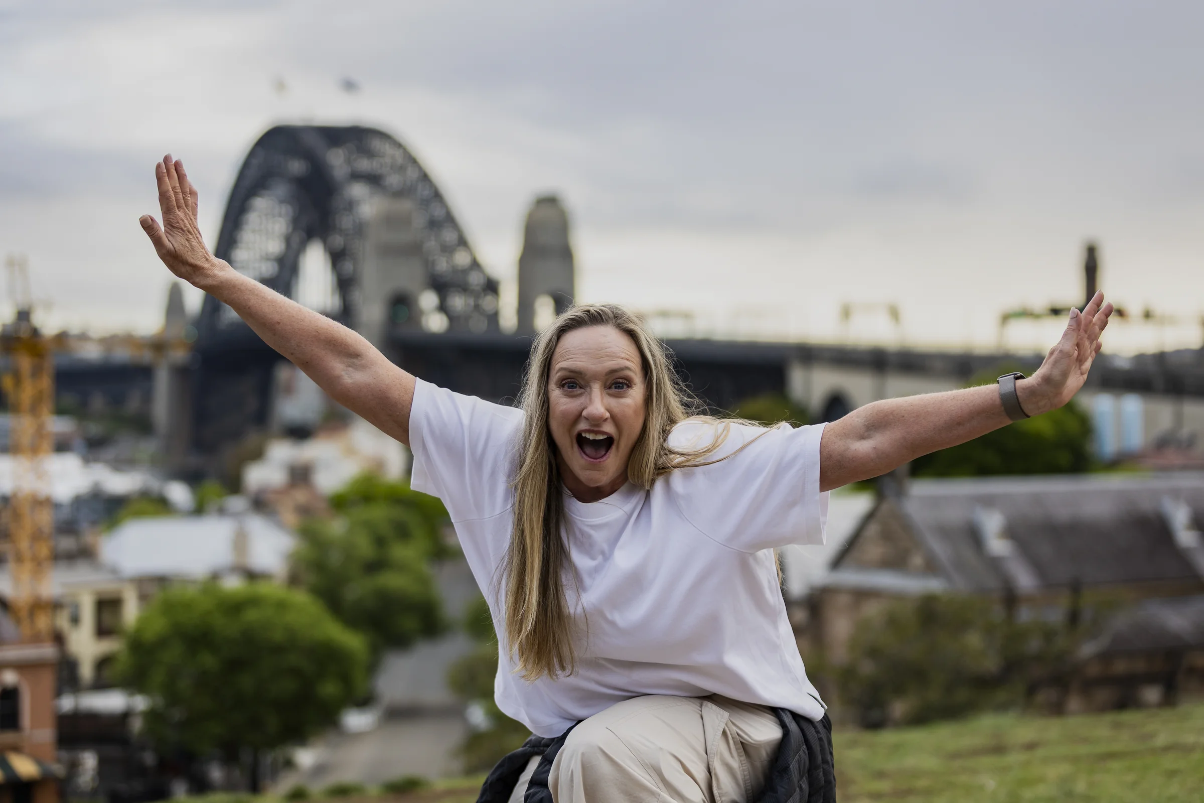 Sue smiling with her arms outstretched and the Harbour Bridge behind her at Observatory Hill