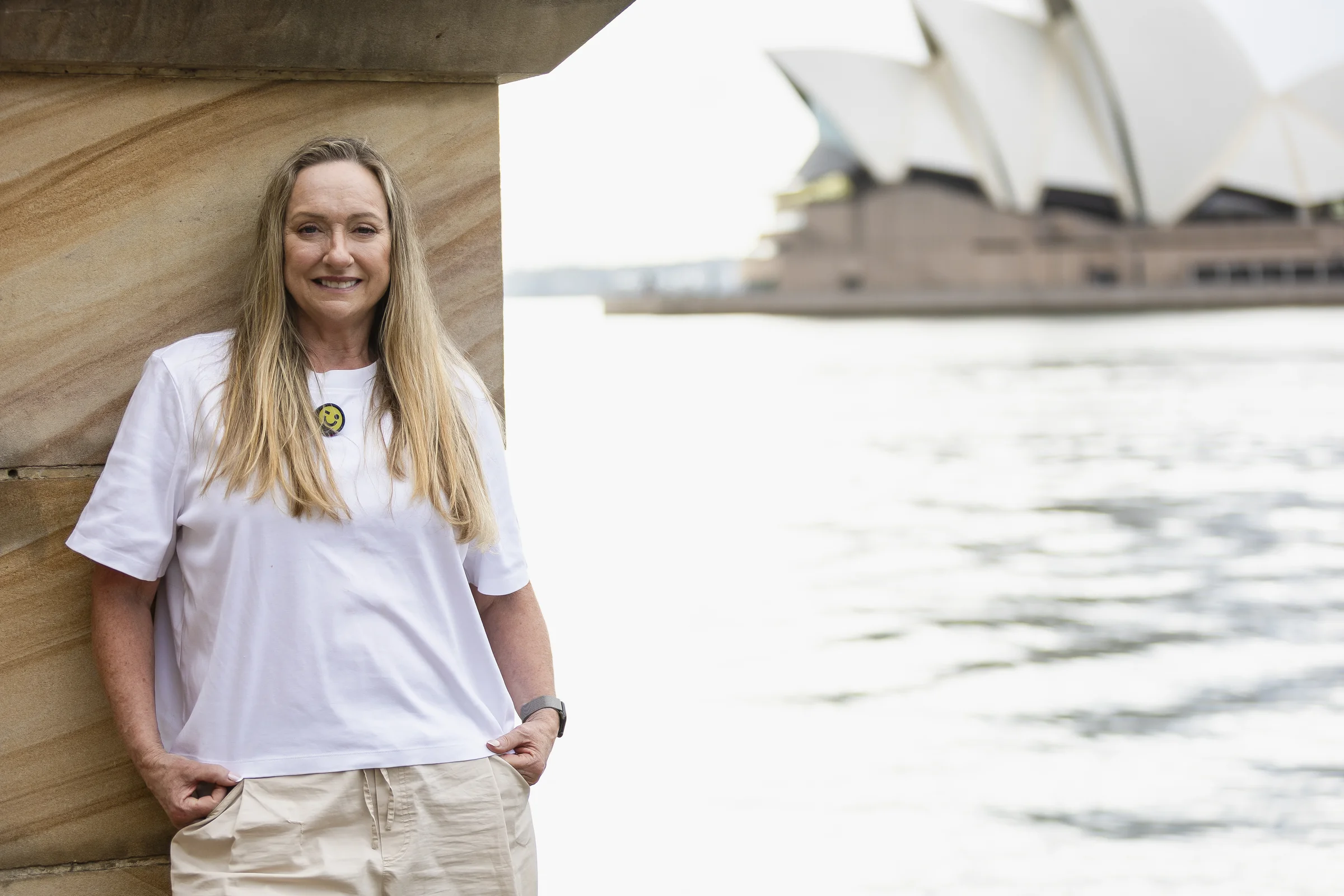 Sue beside the sandstone waterfront structure with the Opera House across the water
