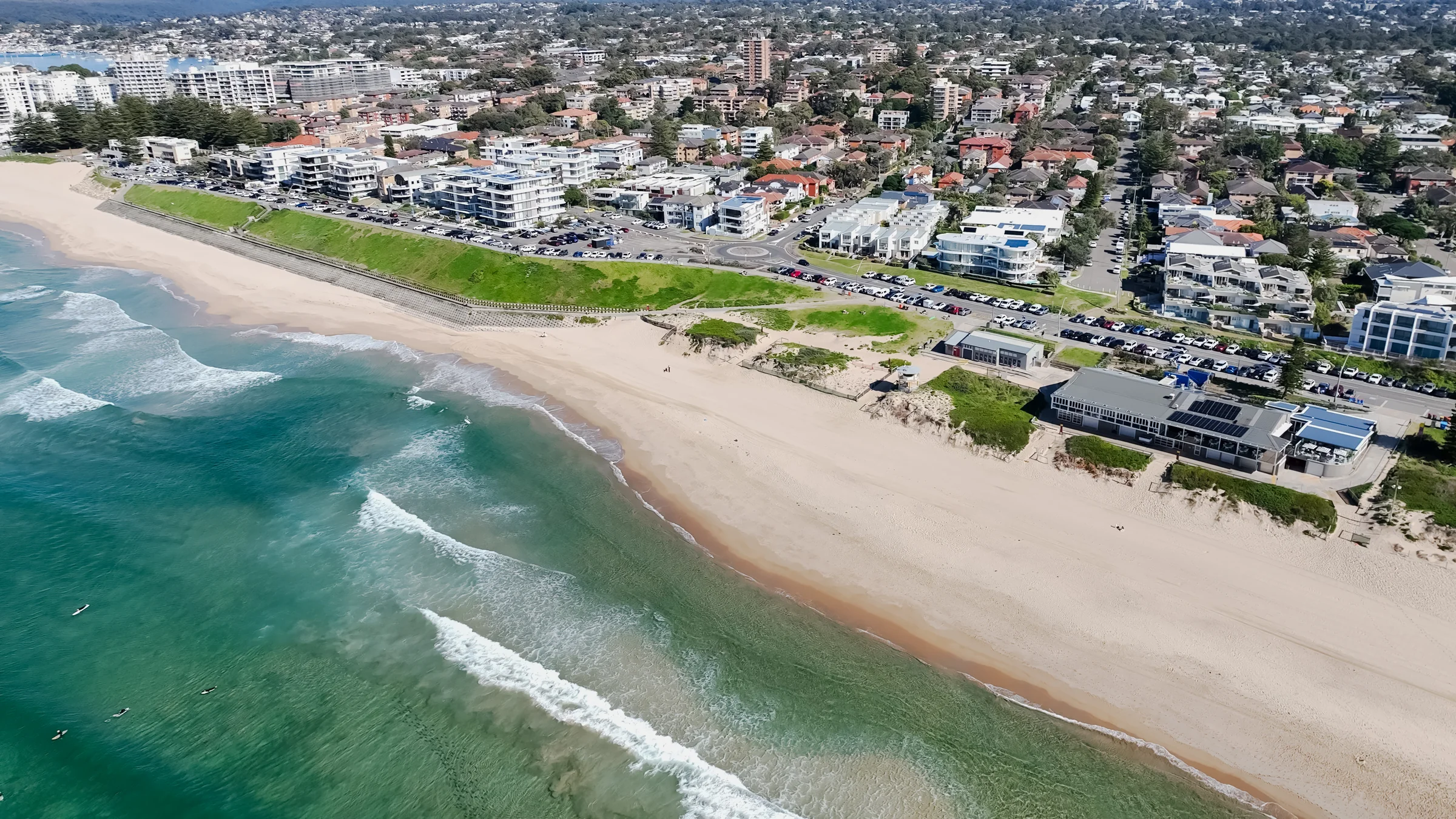 Aerial view of Elouera Beach, its surf club, grassy hill and turquoise surf