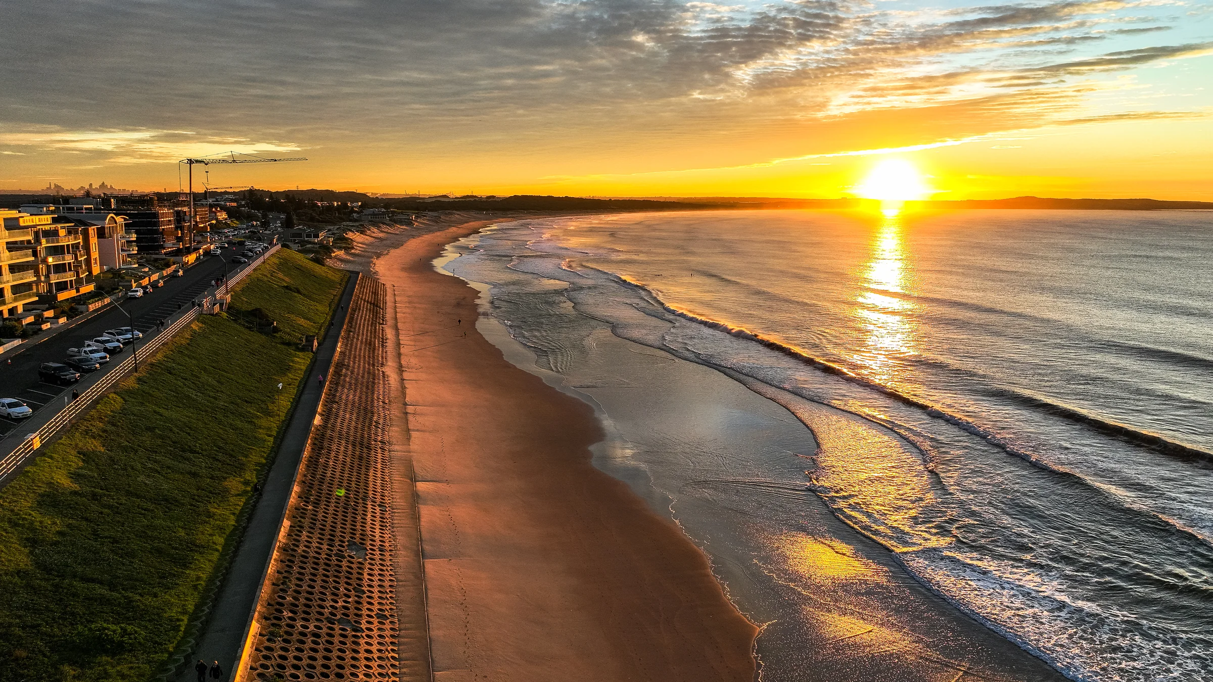Golden sunrise over Elouera Beach with sunlight reflected across the surf and the grassy hill beside the sand