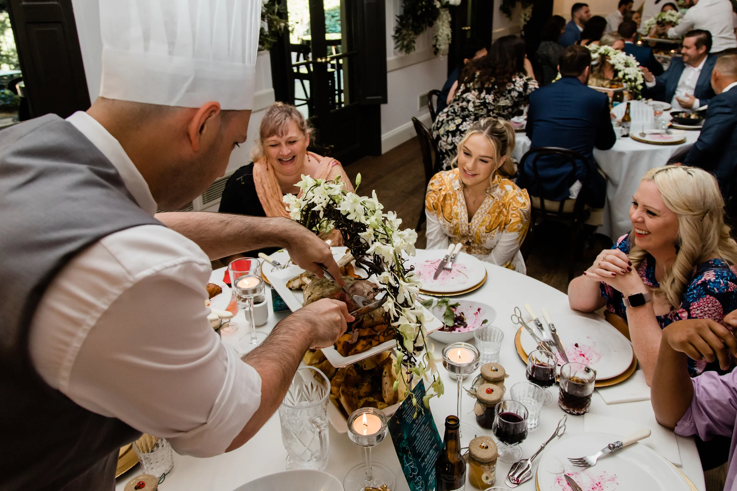 Chef carving and serving food at the table while guests look on