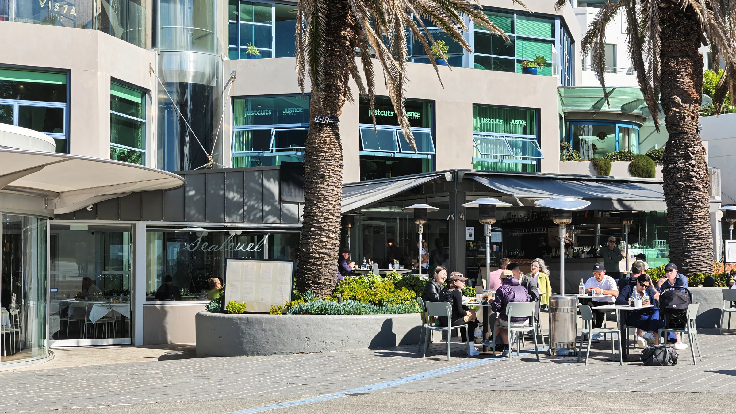 People sitting outside cafés beside palm trees at North Cronulla