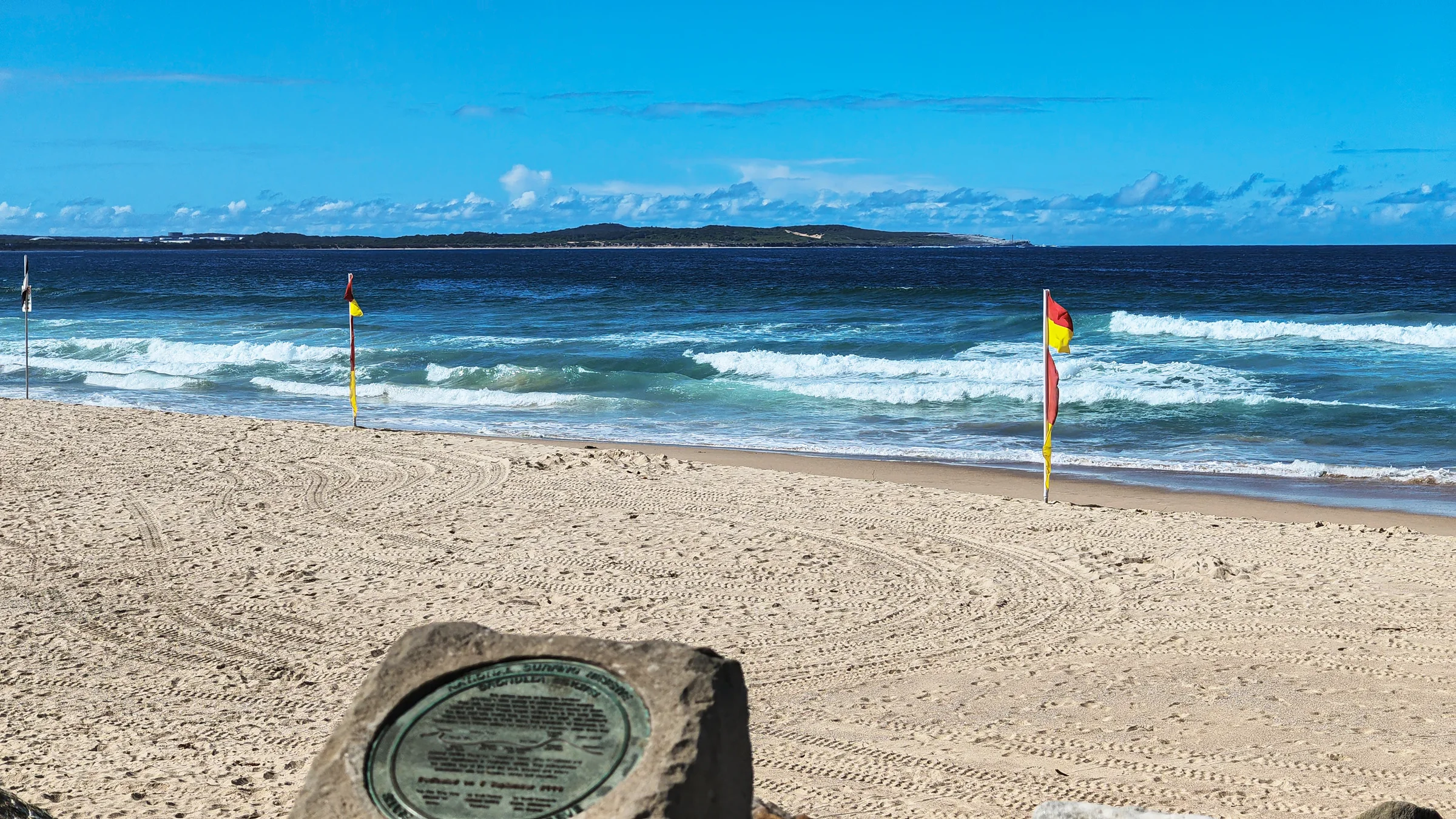 Red and yellow swimming flags on North Cronulla Beach with waves behind them