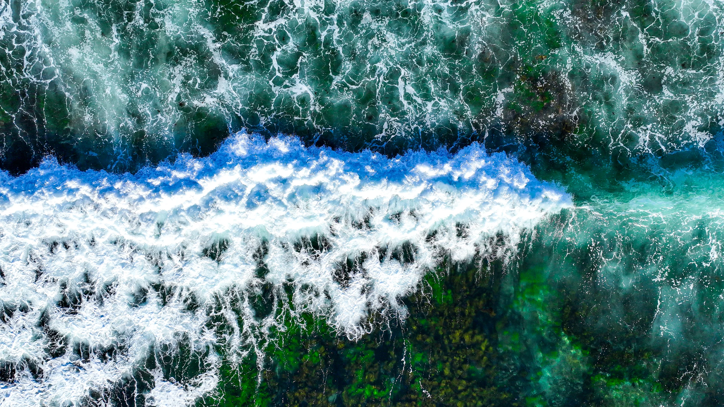 A breaking wave spreading white foam over the turquoise reef at Oak Park