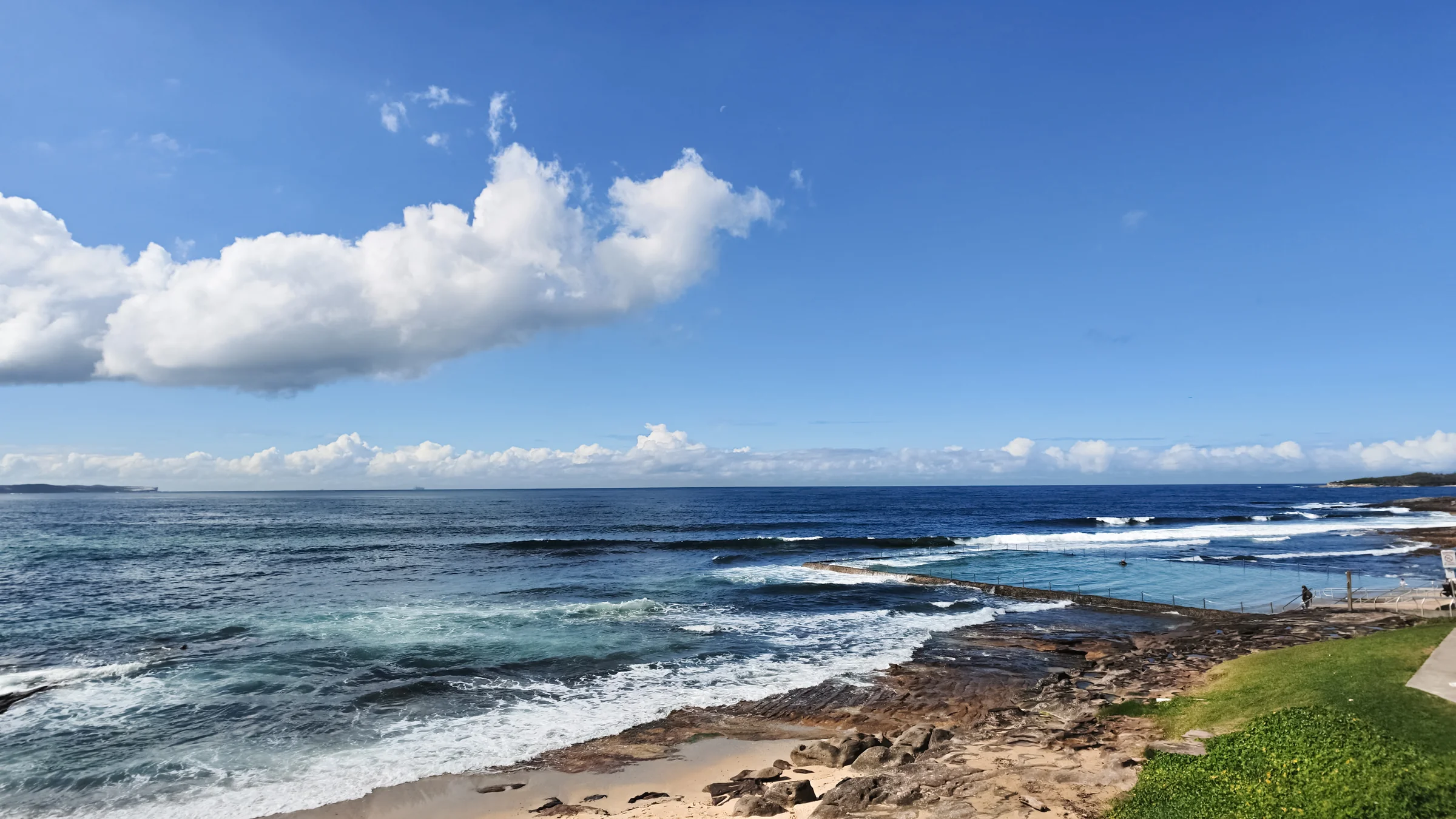 View from the coastal path across Shelly Beach pool and waves along the rocky shoreline