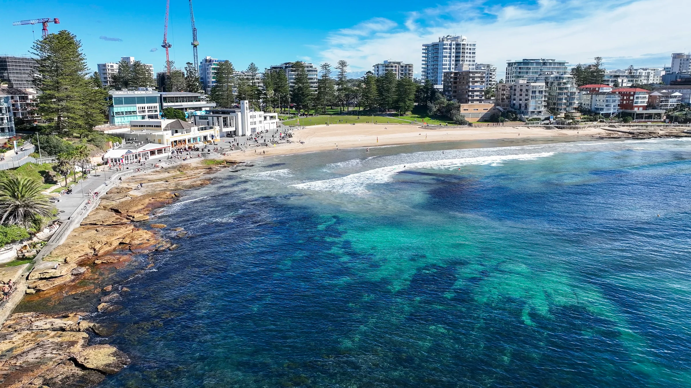 Aerial view of South Cronulla Beach, its surf club, park and clear blue water