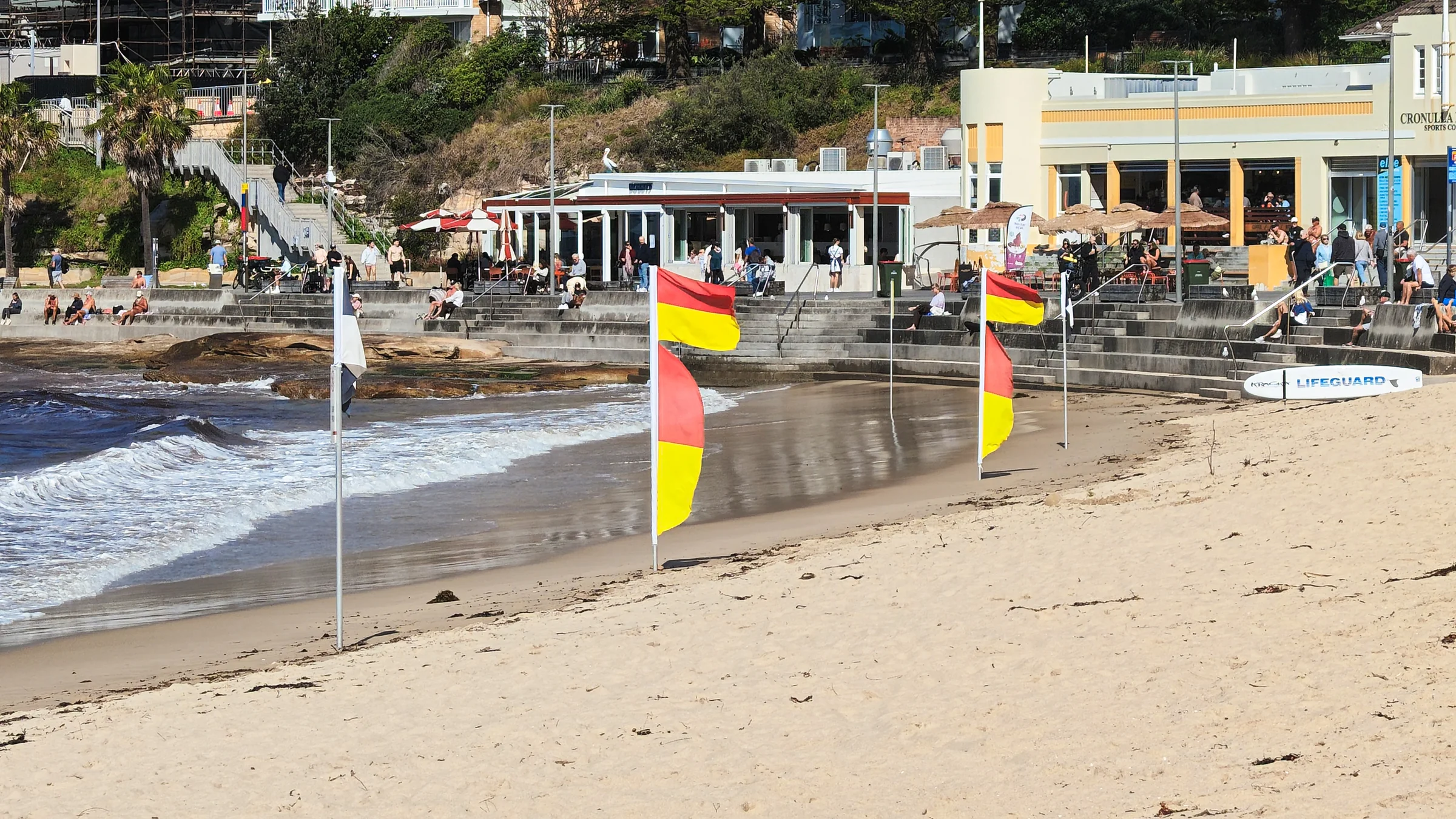 Red and yellow swimming flags on South Cronulla Beach with the pavilion behind