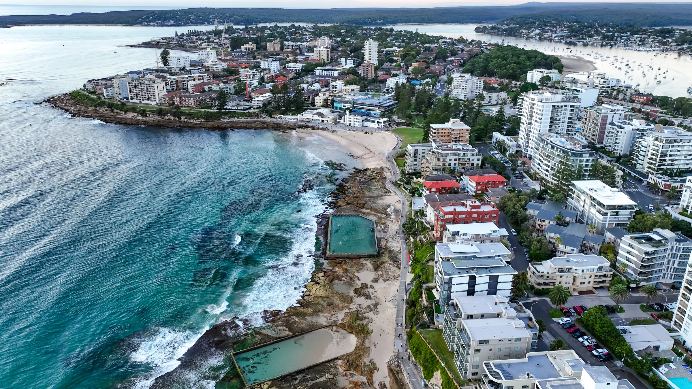 Wide aerial view of both Cronulla ocean pools, South Cronulla Beach and the peninsula