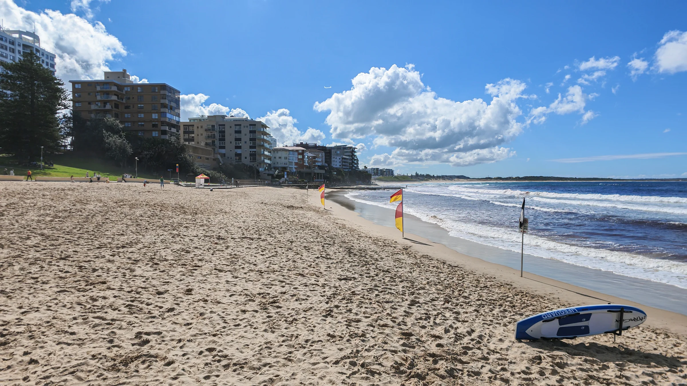 A lifeguard rescue board and flags beside the sand and waves at South Cronulla