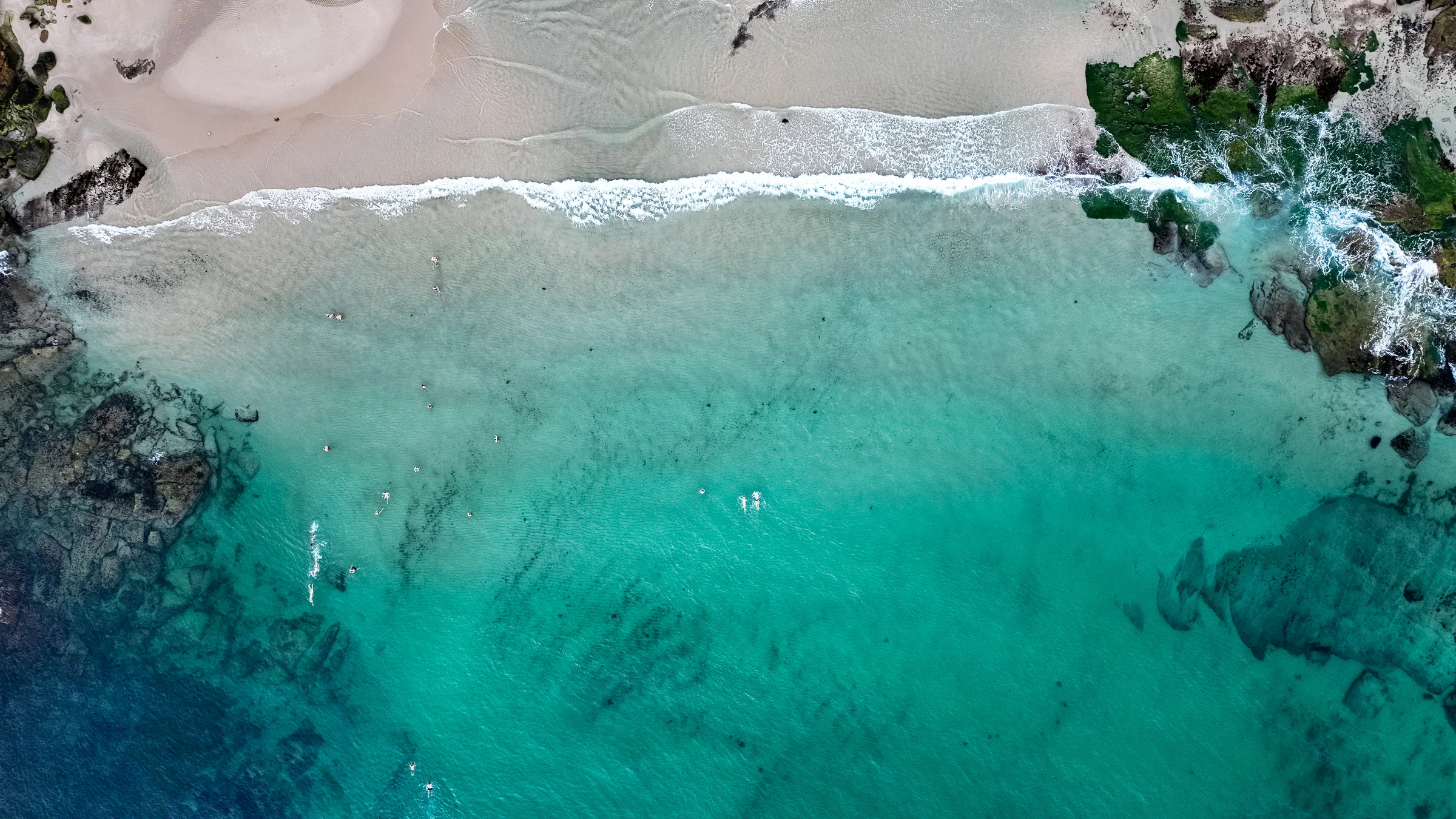 Clear turquoise water, swimmers and small waves beside the sandy shoreline