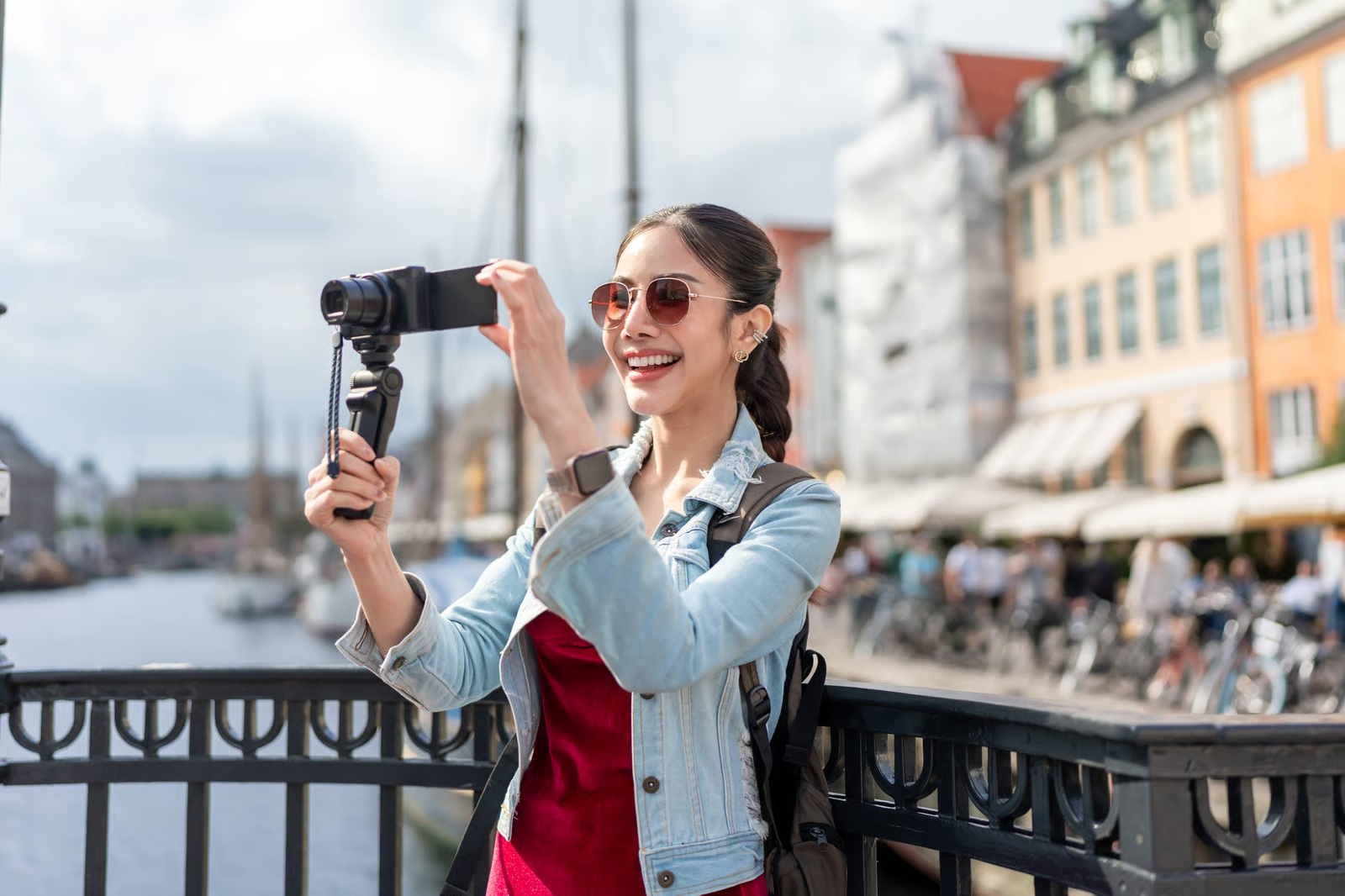 A travel creator recording with a camera beside a canal lined with colourful historic buildings