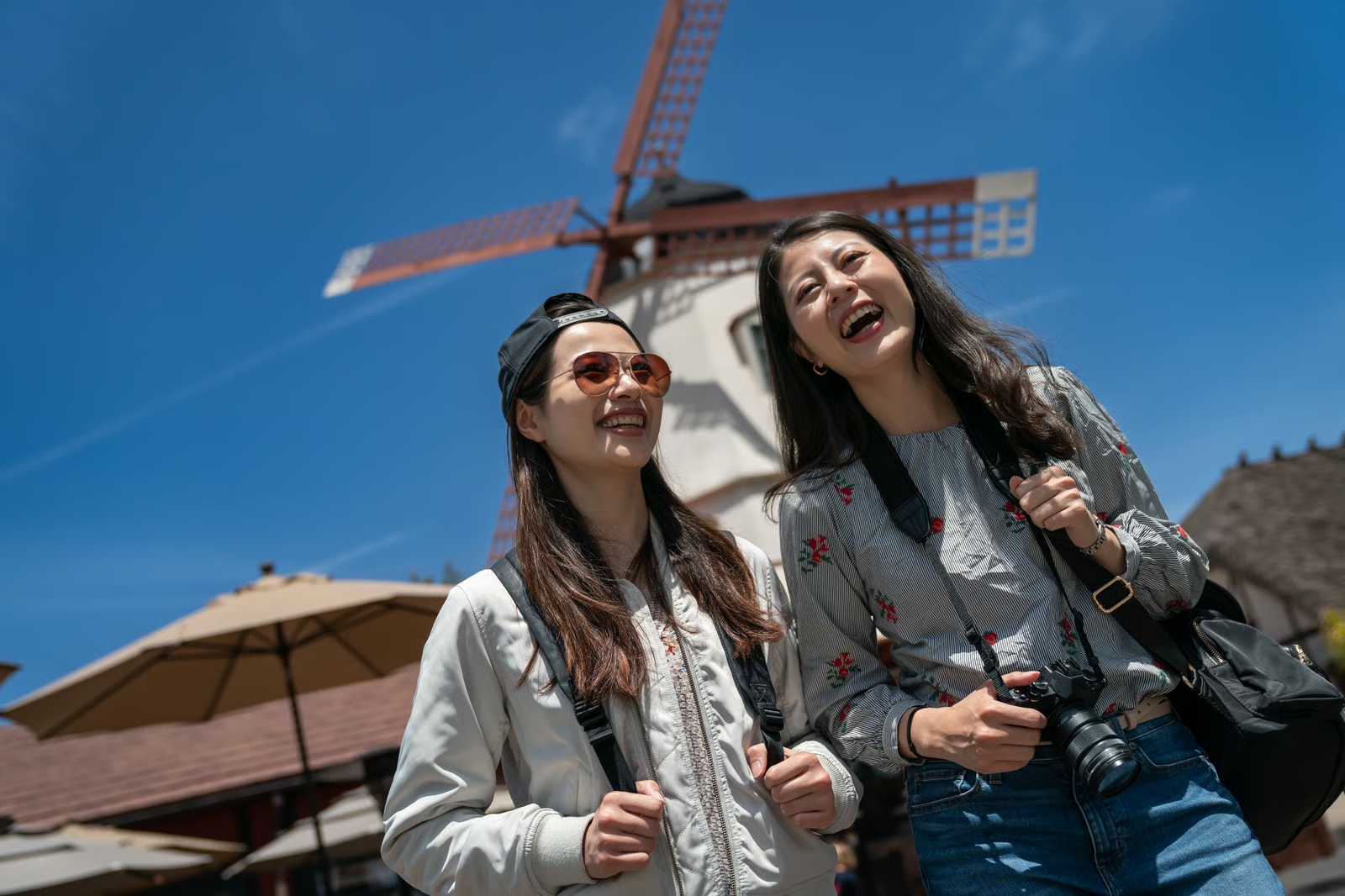 Two friends sightseeing beneath a windmill on a sunny day