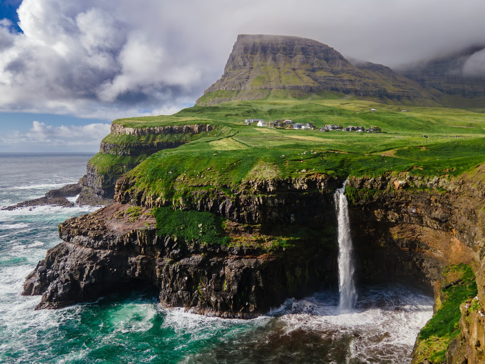 Mulafossur waterfall and the green cliffs of the Faroe Islands