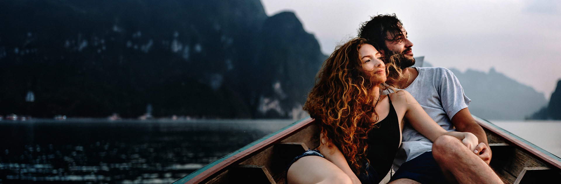 A couple with visible faces taking in a mountainous island landscape from a small boat